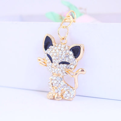 Close-up of a gold-tone rhinestone cat charm hanging from a short chain.
