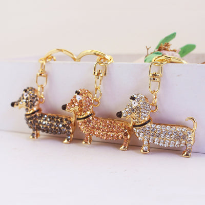 Three gold-tone dachshund keychains covered in white, gray, and peach rhinestones.