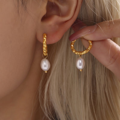 Gold textured and smooth twist hoops with pearl drops held near ear