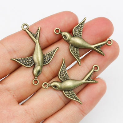 Overview of sculpted flying swallows with a loop at the beak and tail in an antique bronze finish arranged on a light ba
