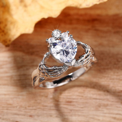 Silver hands holding heart CZ ring on wood