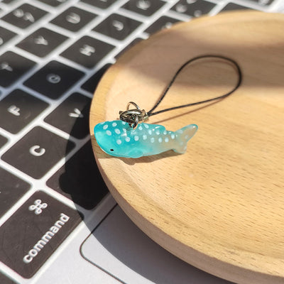 Mini teal polka-dot whale shark phone strap charm on wooden dish