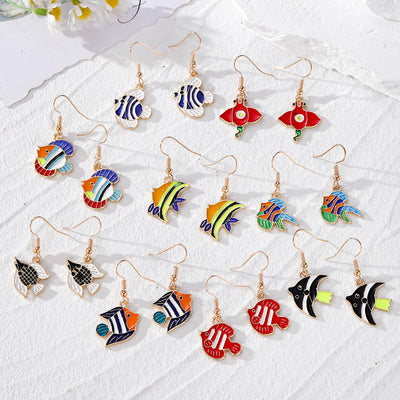 Assorted colorful enamel tropical fish earring pairs arranged on white cloth