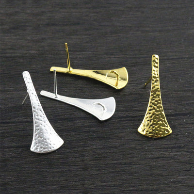 Overview of long tapered textured earring posts in matte gold and silver tones on a light background