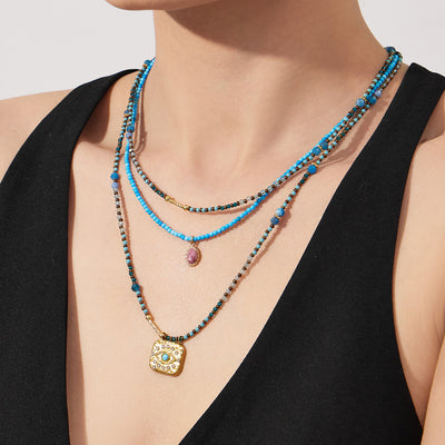 Layered turquoise bead necklaces with pink stone and evil eye on model