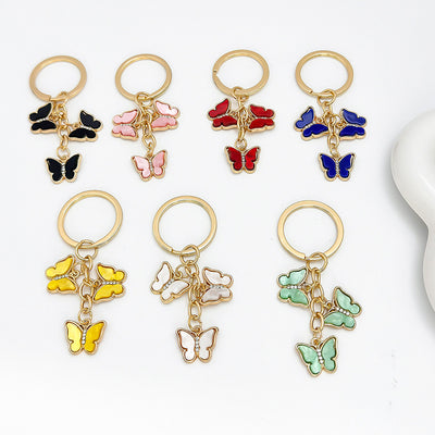 Seven colorways of the triple-butterfly enamel keychain arranged together on a white background, including black, pink,