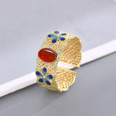 Gold open ring red oval cabochon blue enamel flowers on gray white backdrop