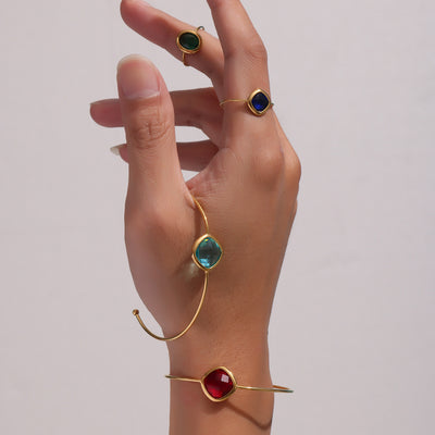 Hand wearing light blue and red cushion glass gold open bangles with rings