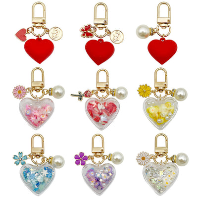 Nine gold-tone clasp keychains display red and clear heart charms in assorted floral designs.
