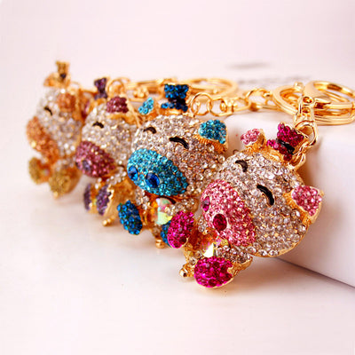 Four rhinestone pig keychains in pink, blue, purple, and gold tones lined up together.