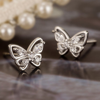 Silver butterfly crystal stud earrings on dark reflective surface