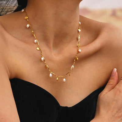 Model wearing gold shell and freshwater pearl charm necklace black top