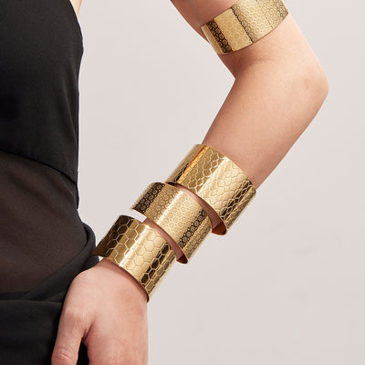 Gold wide cuffs stacked on upper arm and wrist
