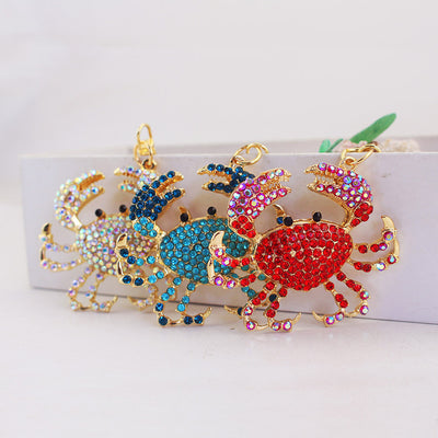 Three rhinestone crab ornaments in iridescent, blue, and red colors stand together.
