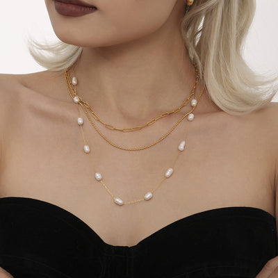 Model wearing layered gold pearl station and paperclip necklaces