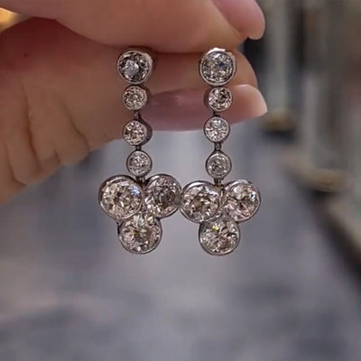 Silver bezel flower drop CZ dangle earrings held close-up outdoor
