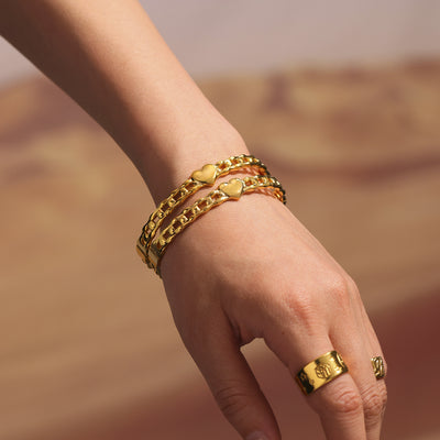 Two gold geometric heart link bangles stacked on wrist