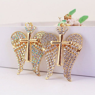 Two gold-tone winged cross charms show clear and iridescent rhinestone styles side by side.