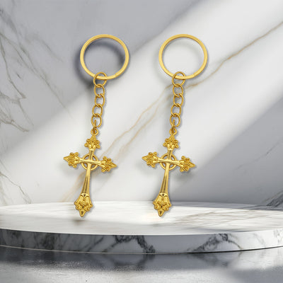 Two gold-tone ornate cross keychains displayed on a marble surface.
