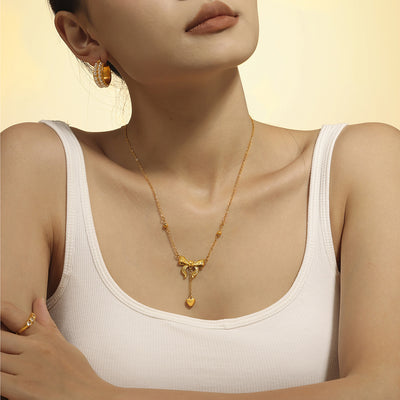 Gold bow heart drop necklace worn on model in white tank