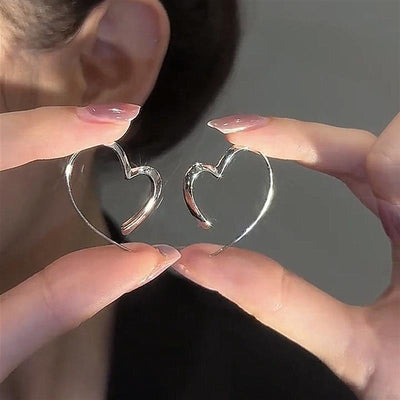 Silver open heart hoop earrings held between fingers near ear