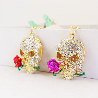 Two gold-tone skull ornaments with clear rhinestones, one pink rose and one red rose.