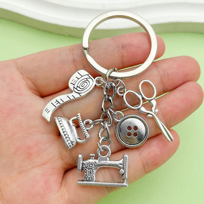 Close-up in a hand of a silver-tone keychain with five dangling sewing motifs.