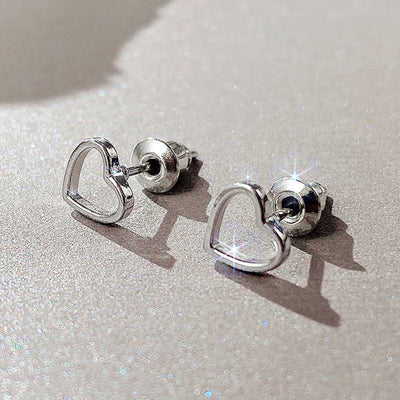 Silver open heart outline studs on glittery beige surface with posts