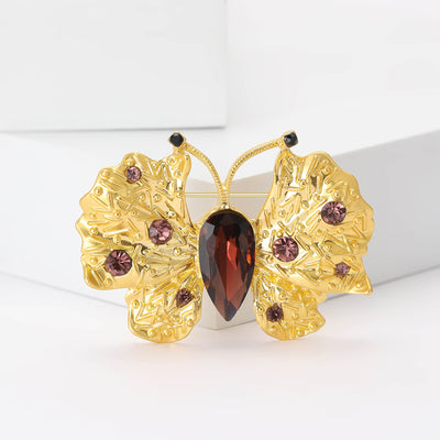 Front view of gold tone butterfly with textured wings and red crystal details