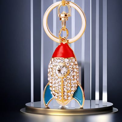 A front product view shows the mini rocket keychain with its visible ornament and hanging hardware.