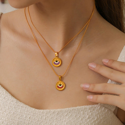 Two gold evil eye enamel pendant necklaces layered on model collarbone