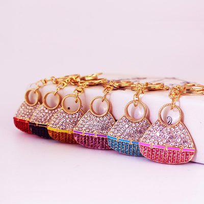 Six gold-tone handbag keychains with red, black, orange, purple, blue, and pink rhinestones arranged in a row.
