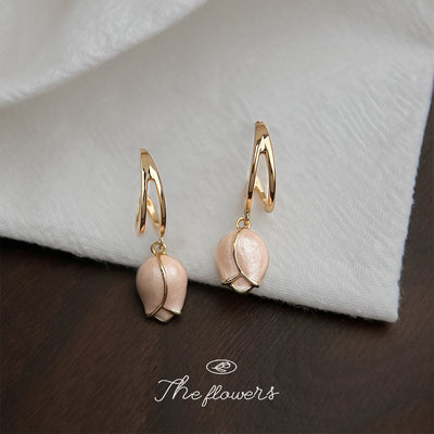 Gold huggie pink tulip charm drops on white cloth wood table