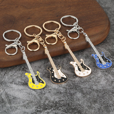Four electric guitar keychains in yellow, black, white, and blue on a gray surface.