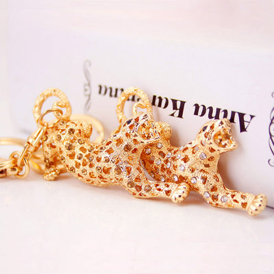 Three gold-tone rhinestone leopard keychains arranged on a pale surface.