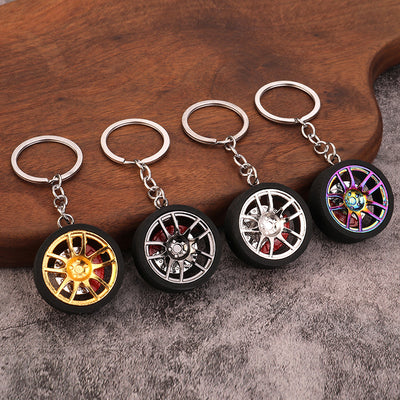 Four wheel-shaped keychains in gold, silver, and iridescent finishes on wood and gray fabric.