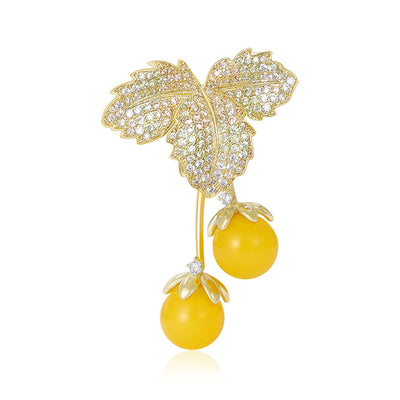 Front view of yellow double cherry brooch with crystal-covered gold leaves against a white background.