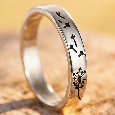Silver dandelion engraved slim band ring on sandy rock close-up