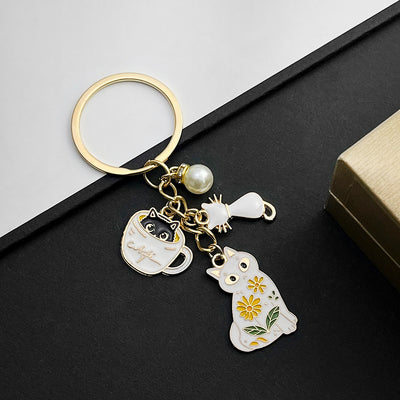 Front product photo of white cat in teacup and faux pearl enamel charm keychain showing the pictured design arrangement