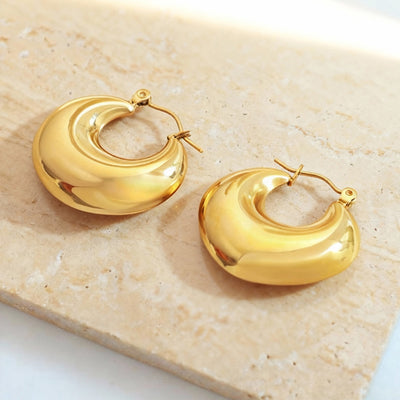 Gold thick open crescent hoop earrings on stone surface