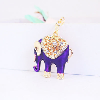 Purple elephant charm standing on a white surface with a gold-tone saddle and clear stones.