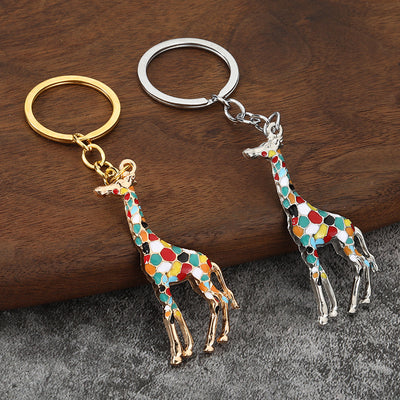 Two multicolor giraffe keychains with gold-tone and silver-tone finishes on a wood surface.