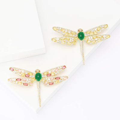 Grouped view of gold tone dragonfly brooch with green oval body and crystal tail arranged together.