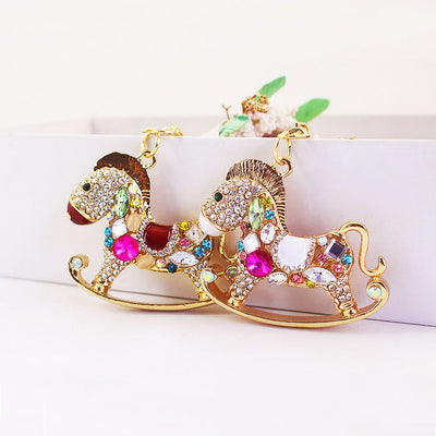 Two gold-tone rocking horse charms with white and brown details stand side by side.