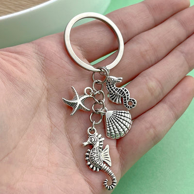 Image 1 showing a hand holding a silver keychain with sea shells.