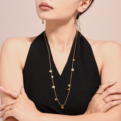 Model in black top wearing long gold hammered disc station necklace layered