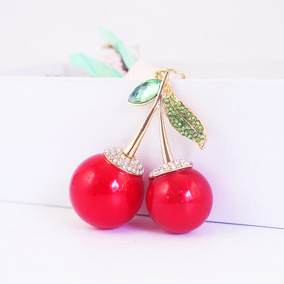 Two glossy red cherry charms with green leaf accents resting against a white box.