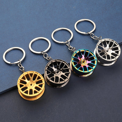 Four wheel rim keychains in gold, gunmetal, rainbow and silver finishes on a dark surface.