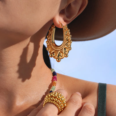 Gold ornate hollow hoop earring worn on ear with hat brim shadow