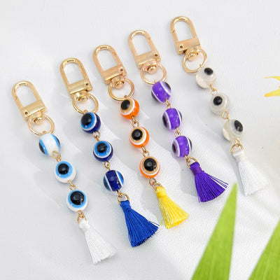 Row of five evil eye keychains in blue, orange, purple and white with matching tassels